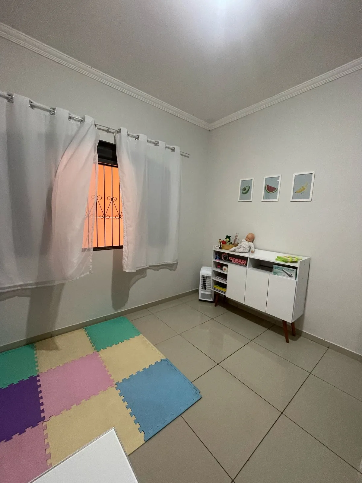 Sala com tapete colorido de encaixe, cortinas claras e um móvel baixo com brinquedos